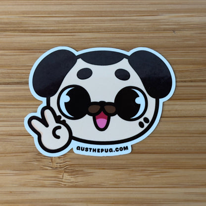 Cartoon dog sticker making a peace sign on a wooden surface